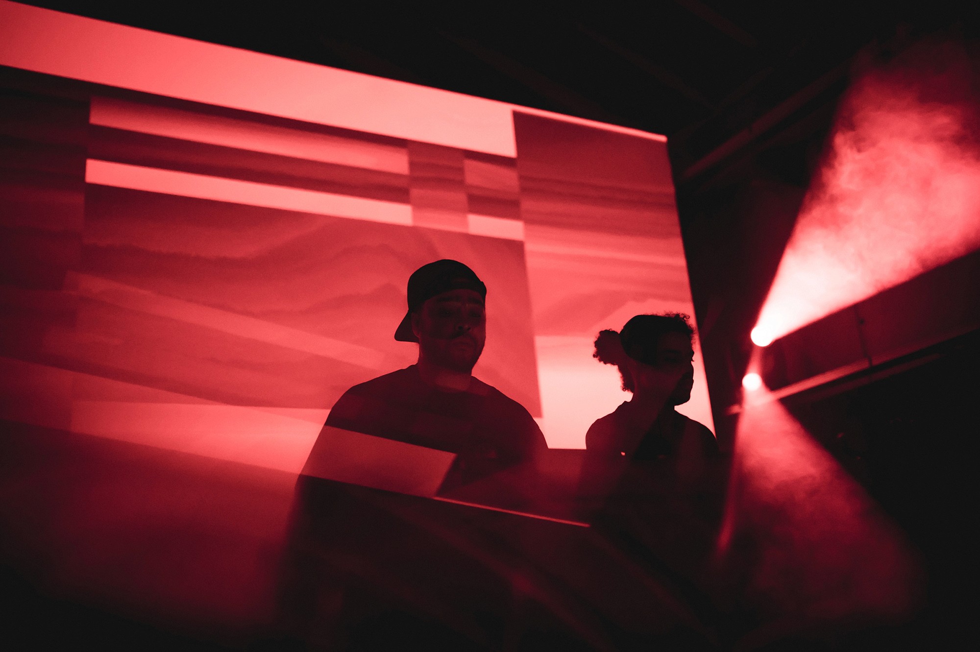 Backlit silhouette of the group Black Rave Culture on a flat red projection.