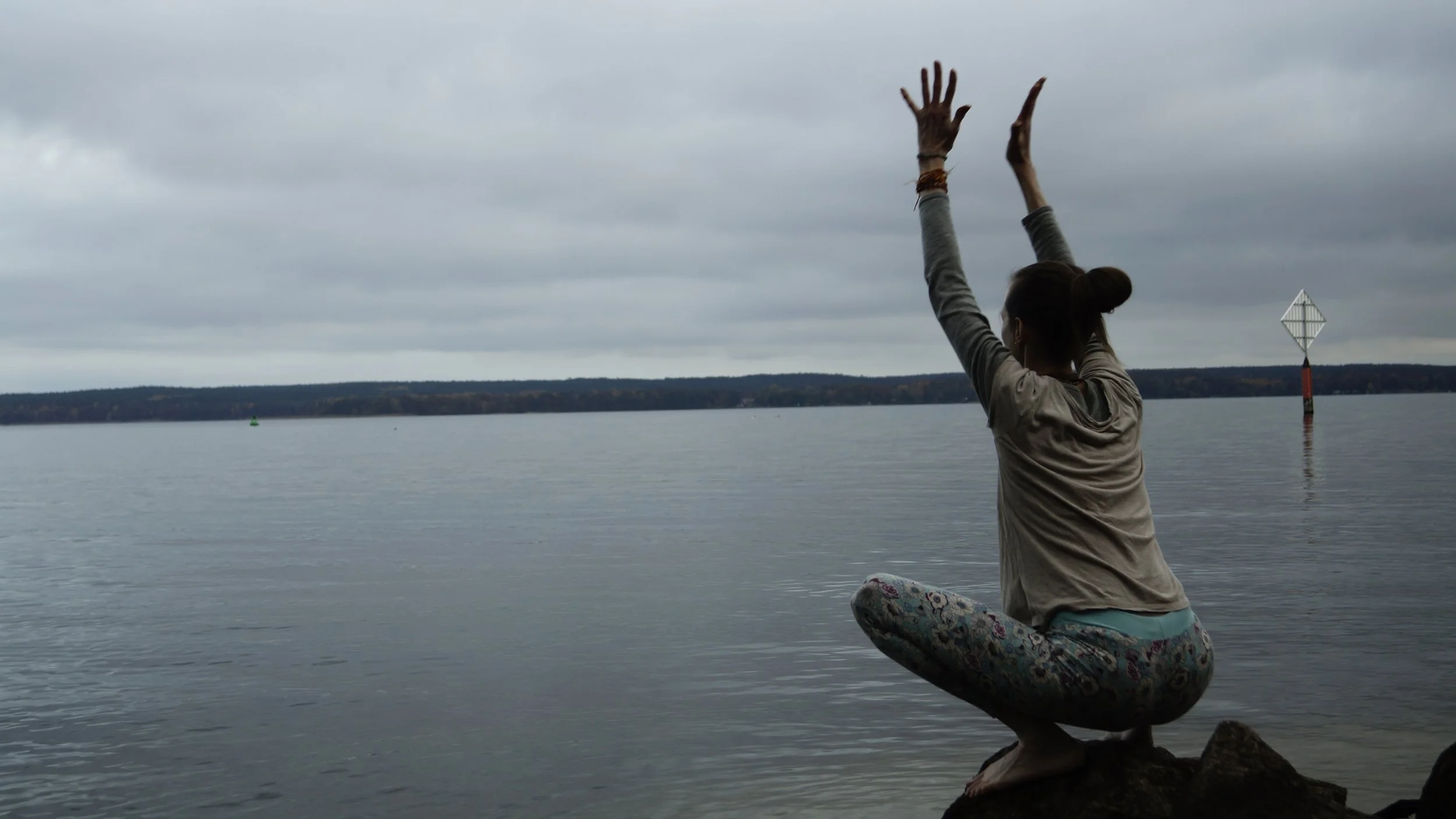 Yogalehrerin (Karina Gaurangi Schmuck) am Wasser in tiefer Hocke mit gestreckten Armen über dem Kopf