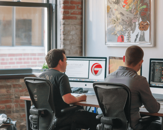 Two people working at computers in a brick-walled office