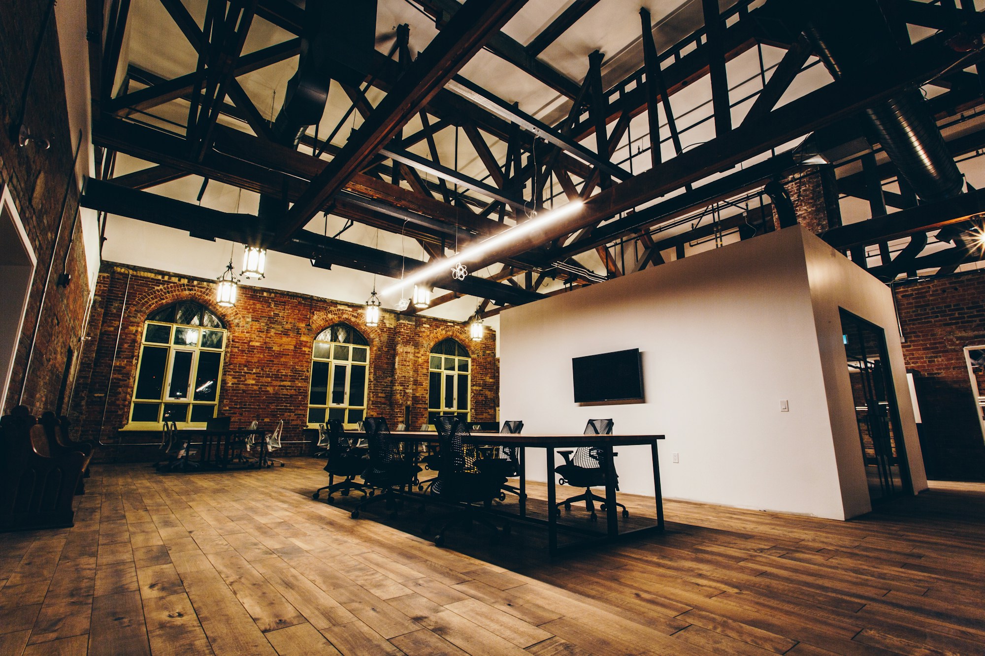 A converted brick warehouse with tall arched windows, steel roof trusses, wood floors and rows of desks