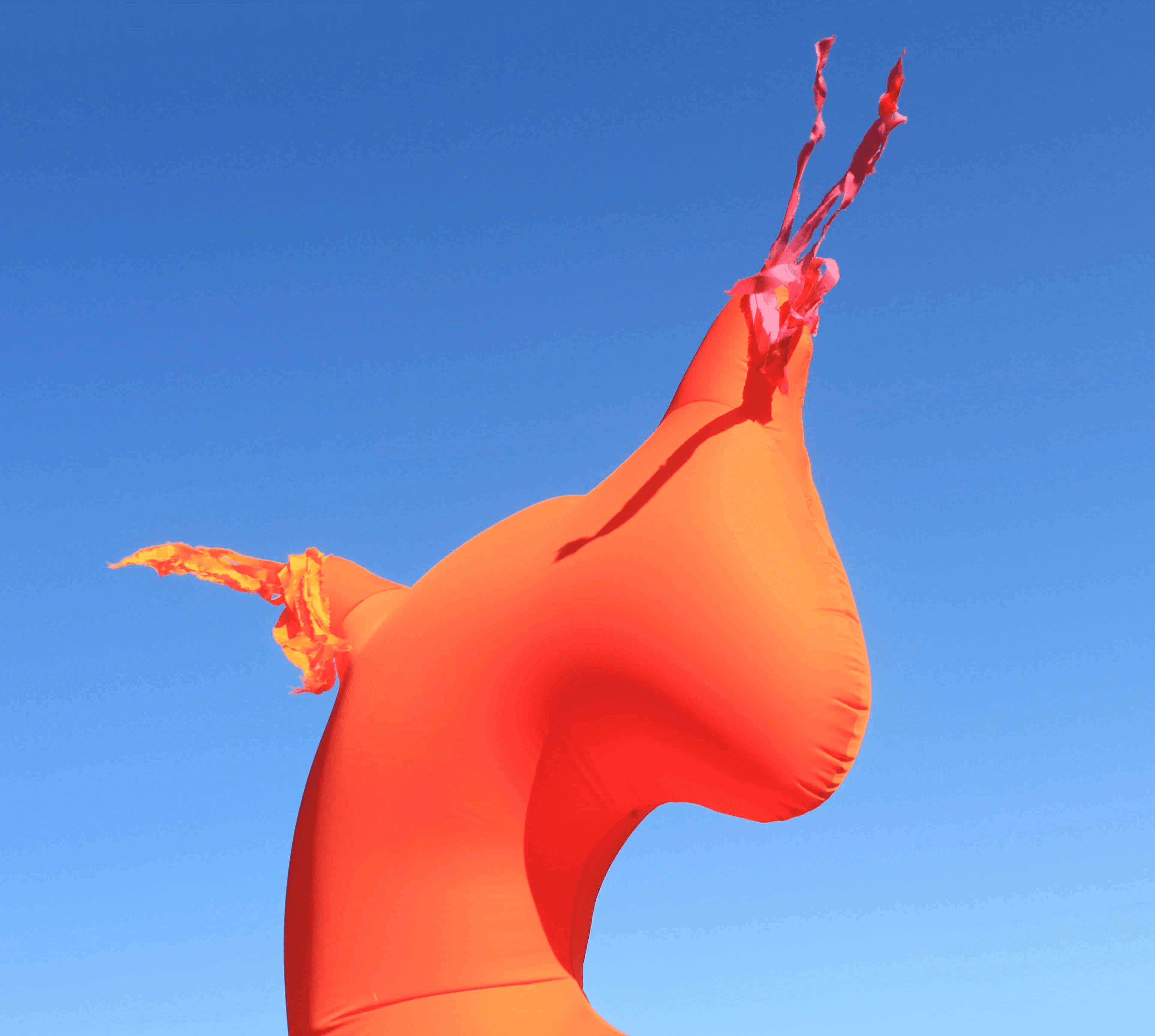 A stylized, bright orange creature with prominent appendages against a clear blue sky.