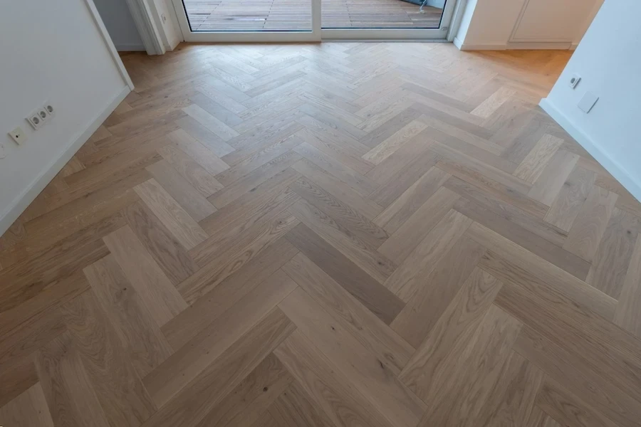 Zimmer mit großer Glasfront und frisch verlegtem Fischgrät-Parkettboden in warmem Holzton.