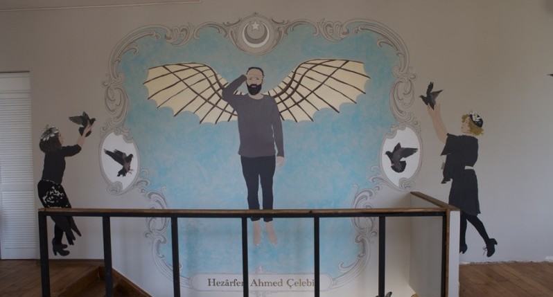 A wall paining of a man with wings. On his sides two women with pigeons in their hands and another two pigeons in white circles.