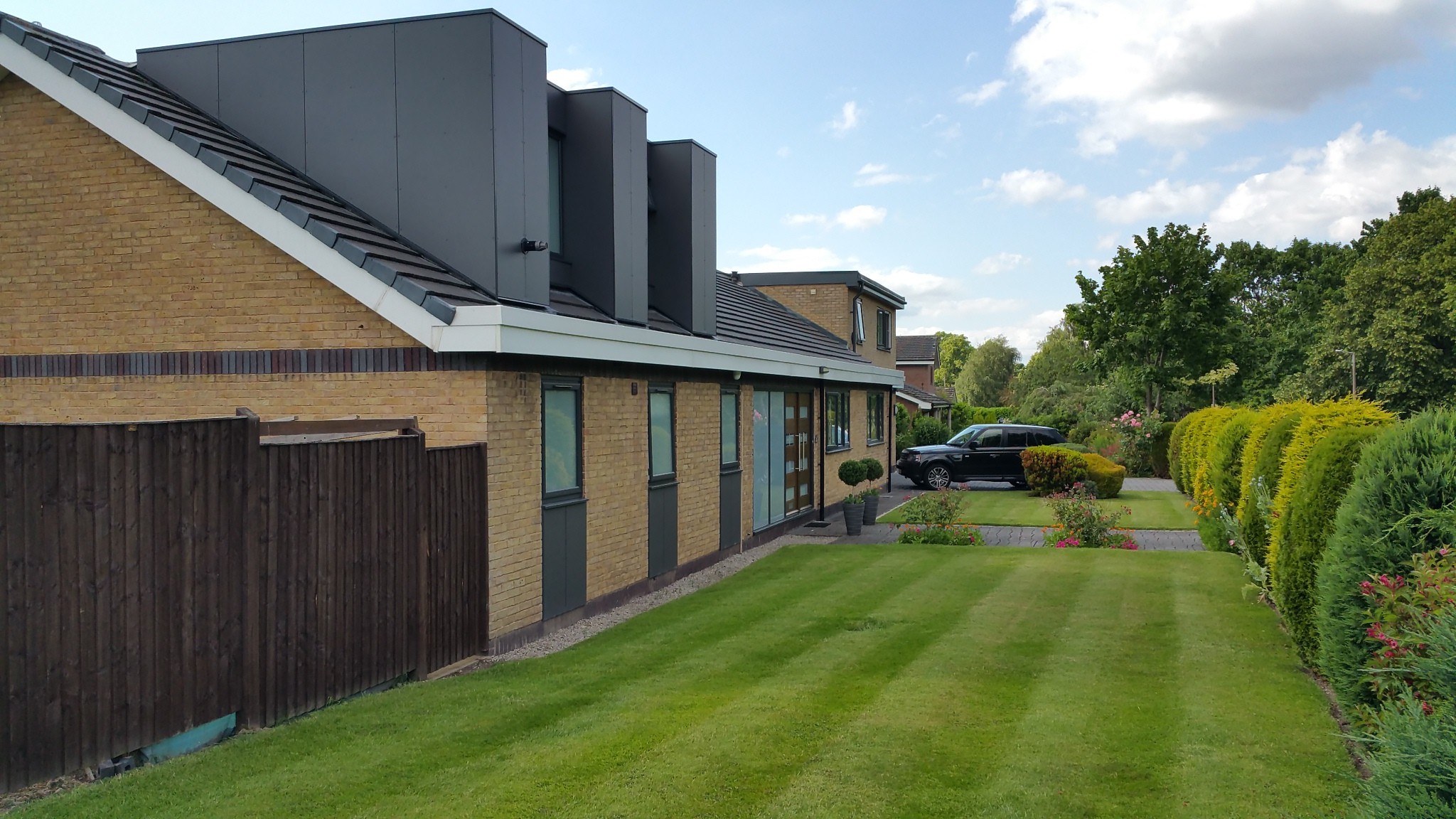 Side elevation of remodelled bungalow showing multiple modern roof pods, updated cladding, and landscaped front garden.