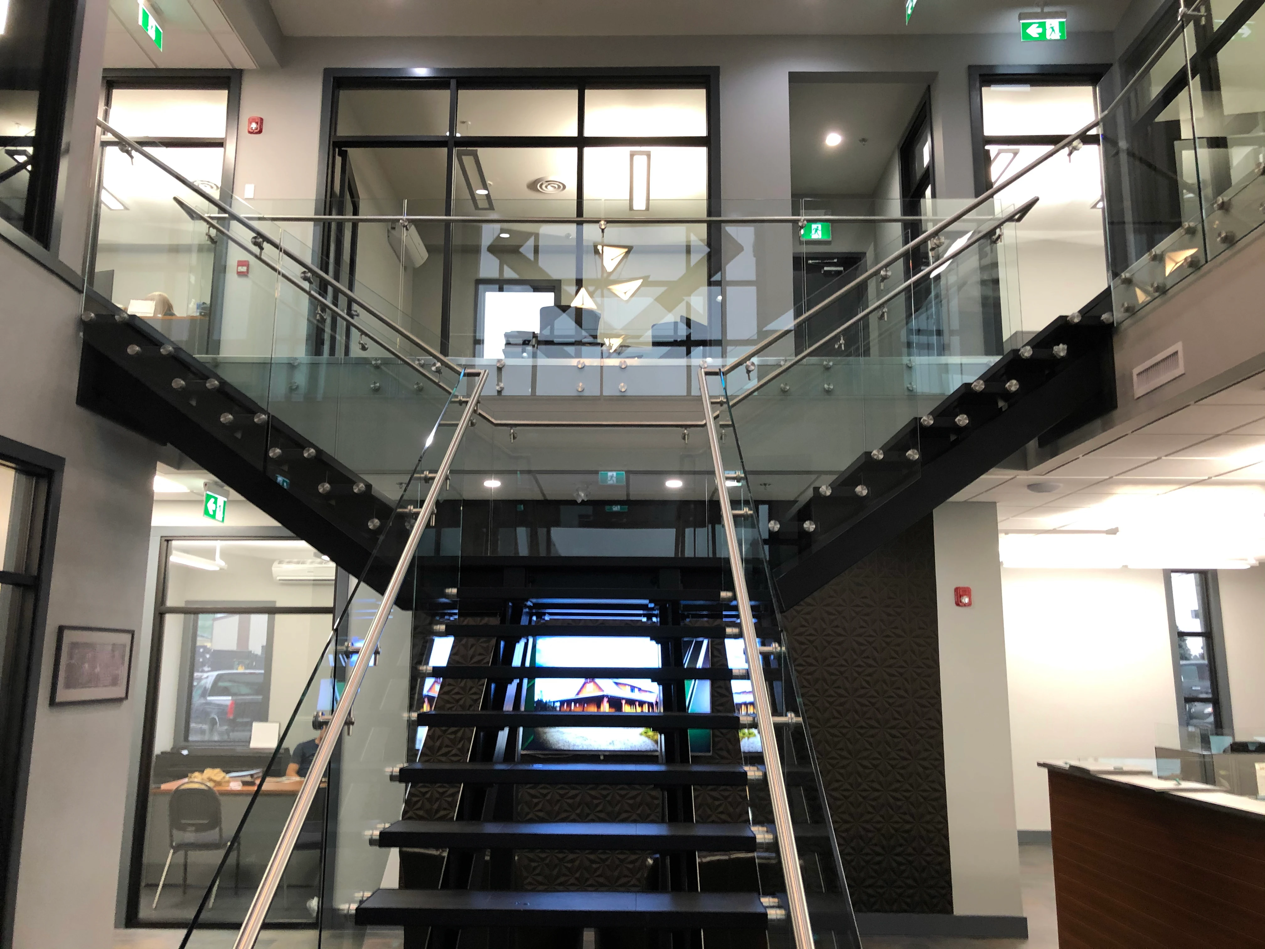 Glass guardrail system with stainless posts and handrail along a floating staircase in a BC commercial lobby.