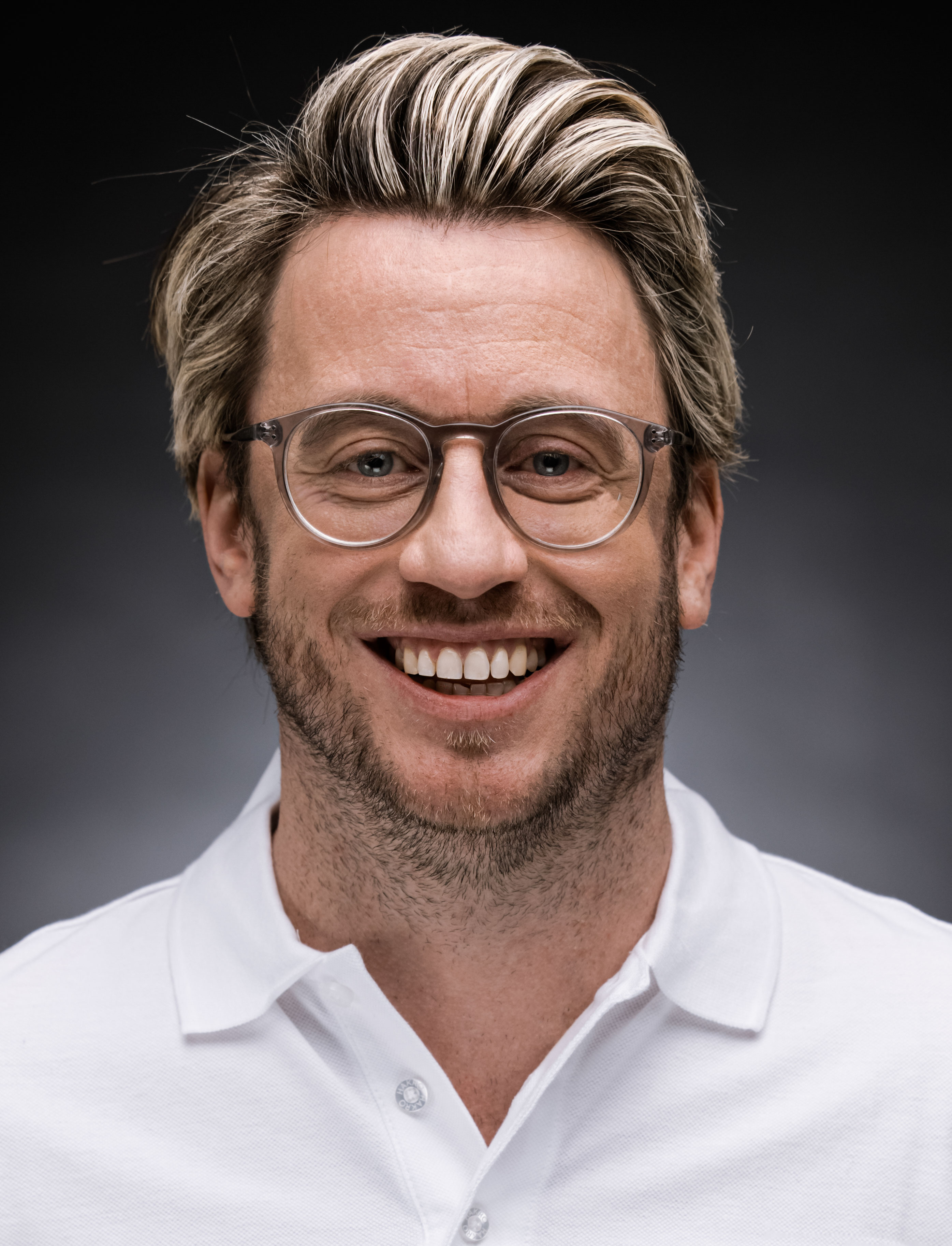 Mann mit weißen Hemd blickt lächelnd in die Kamera.