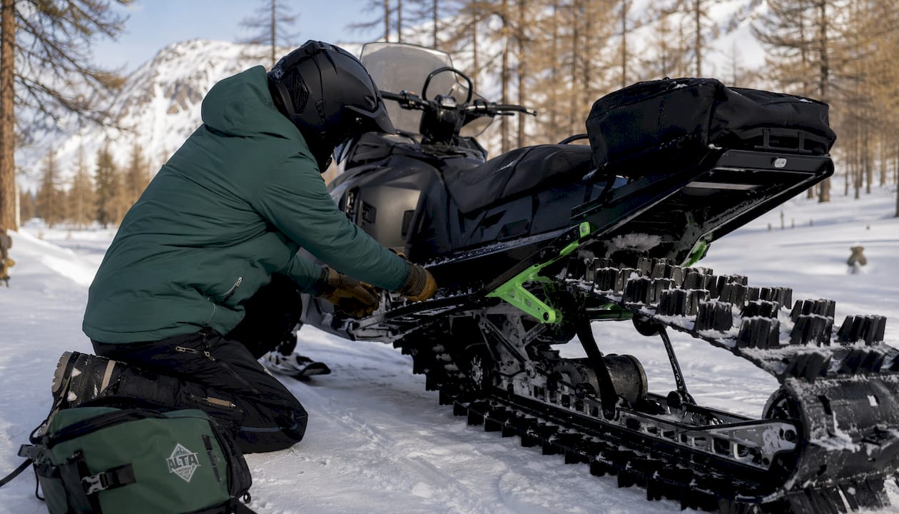 A guide adjusting a snowmobile in snowy backcountry