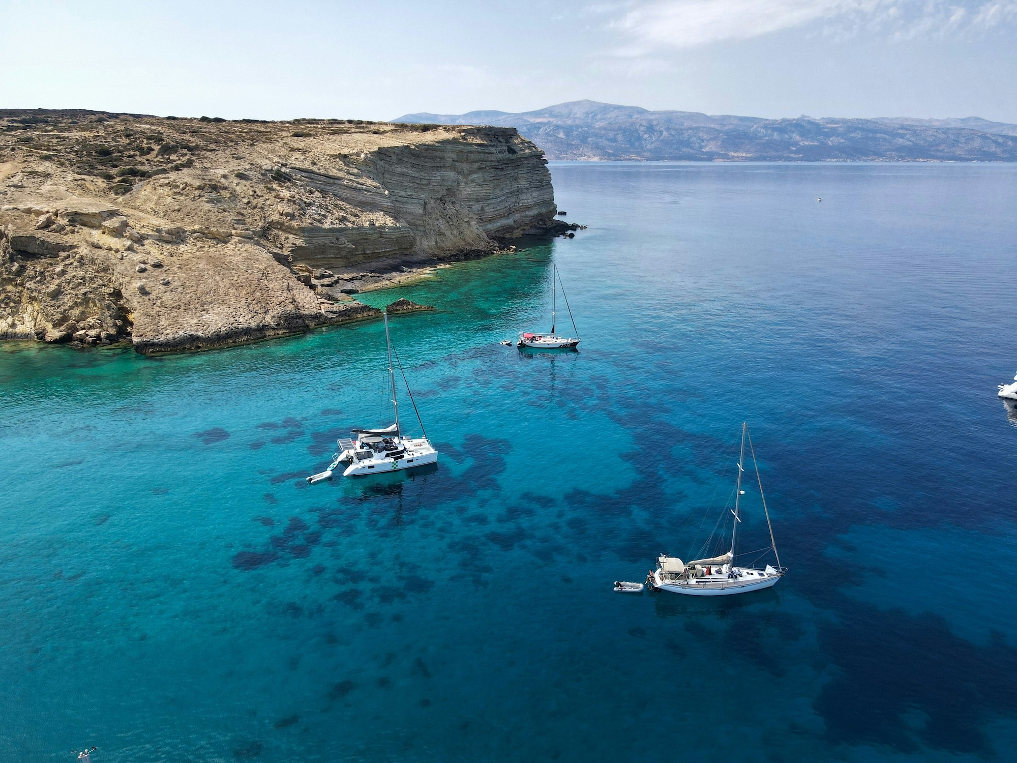 Aerial view of yachts anchored in a pristine white sand beach bay with turquoise waters in the Greek islands