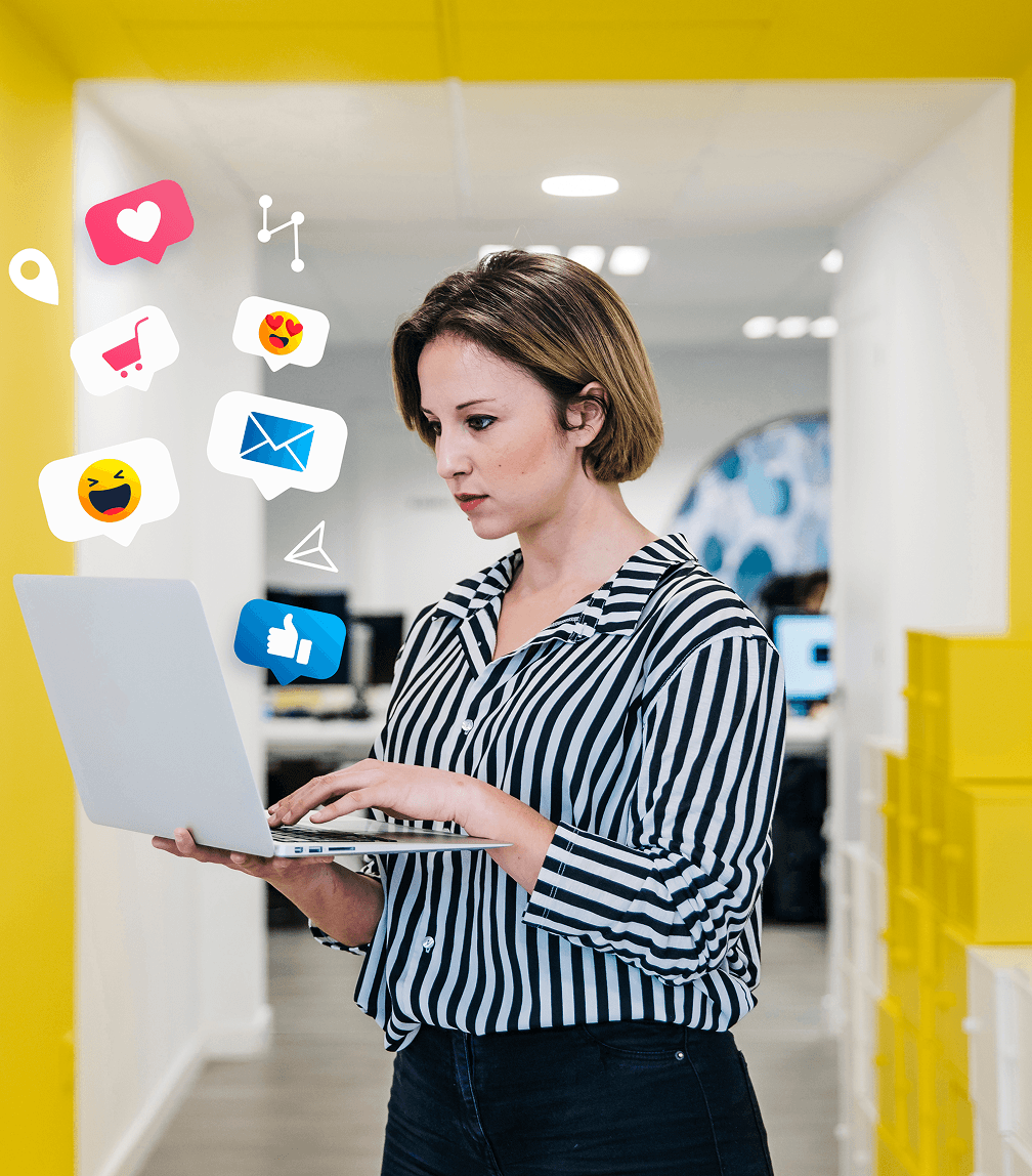 A woman stands in an office, with social media icons emerging from her laptop, symbolizing digital connectivity and engagement.
