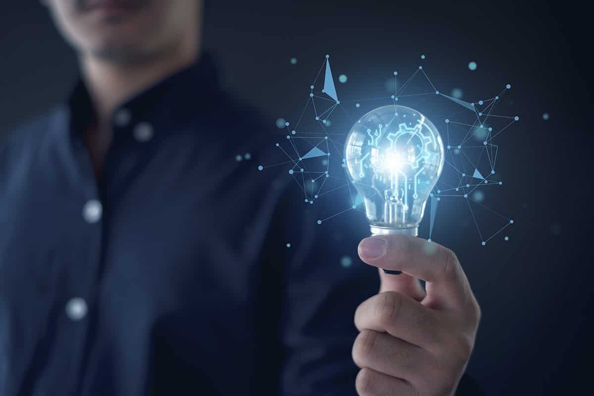 A person in a dark setting holds a glowing light bulb, symbolizing ideas or innovation.