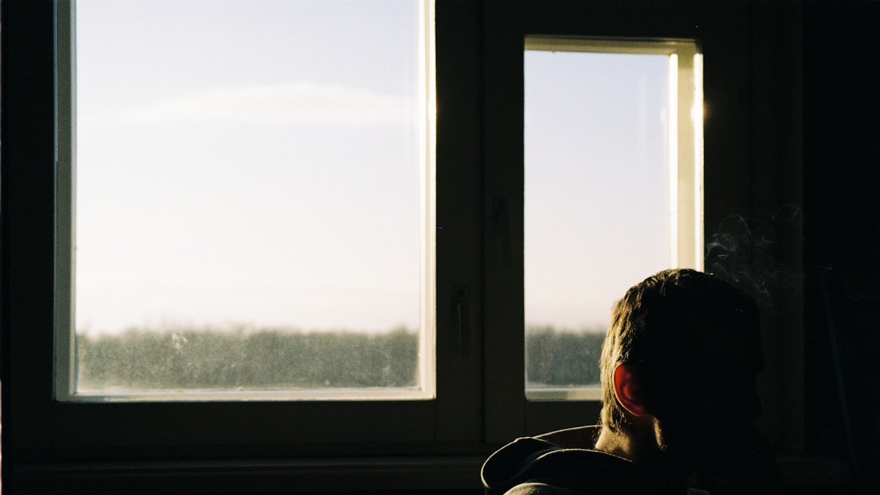 Person sitting by a window deep in thought, reflecting on longing and obsessive feelings | Photo by Jana Shnipelson on Unsplash