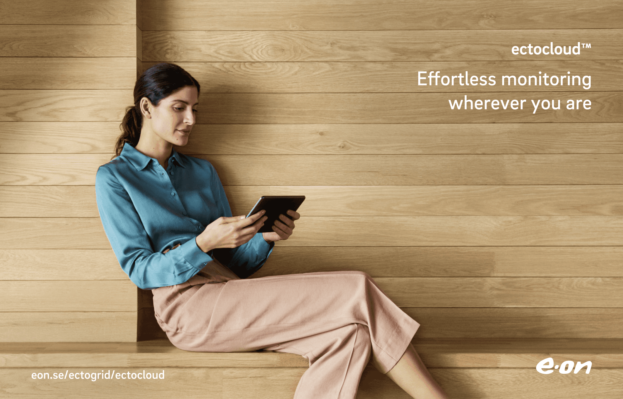 Women sitting down viewing an ipad. Oak wall and bench