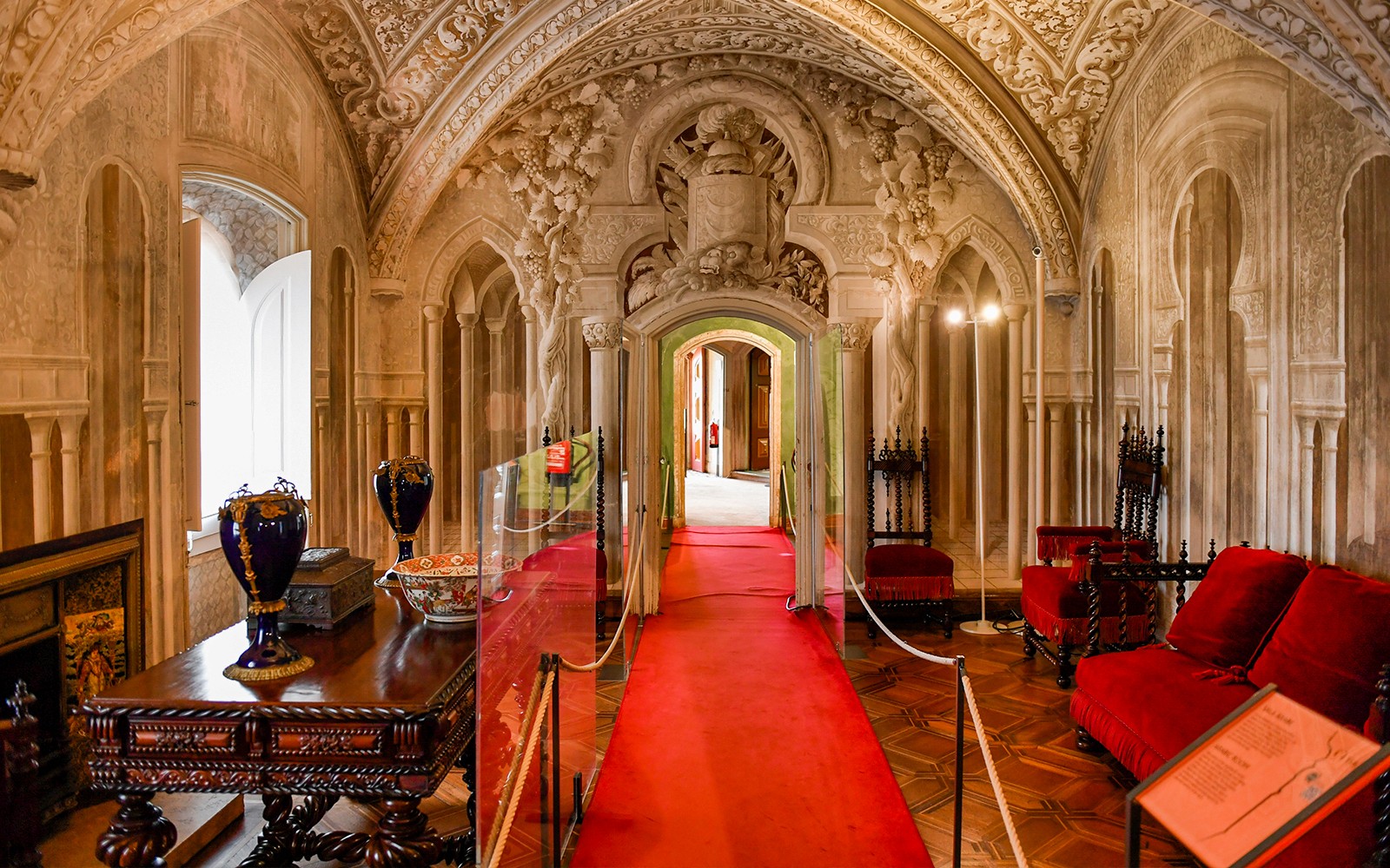 Lorong dalaman Istana Pena di Sintra, Portugal, menampilkan lengkungan hiasan dan tempat duduk baldu merah.