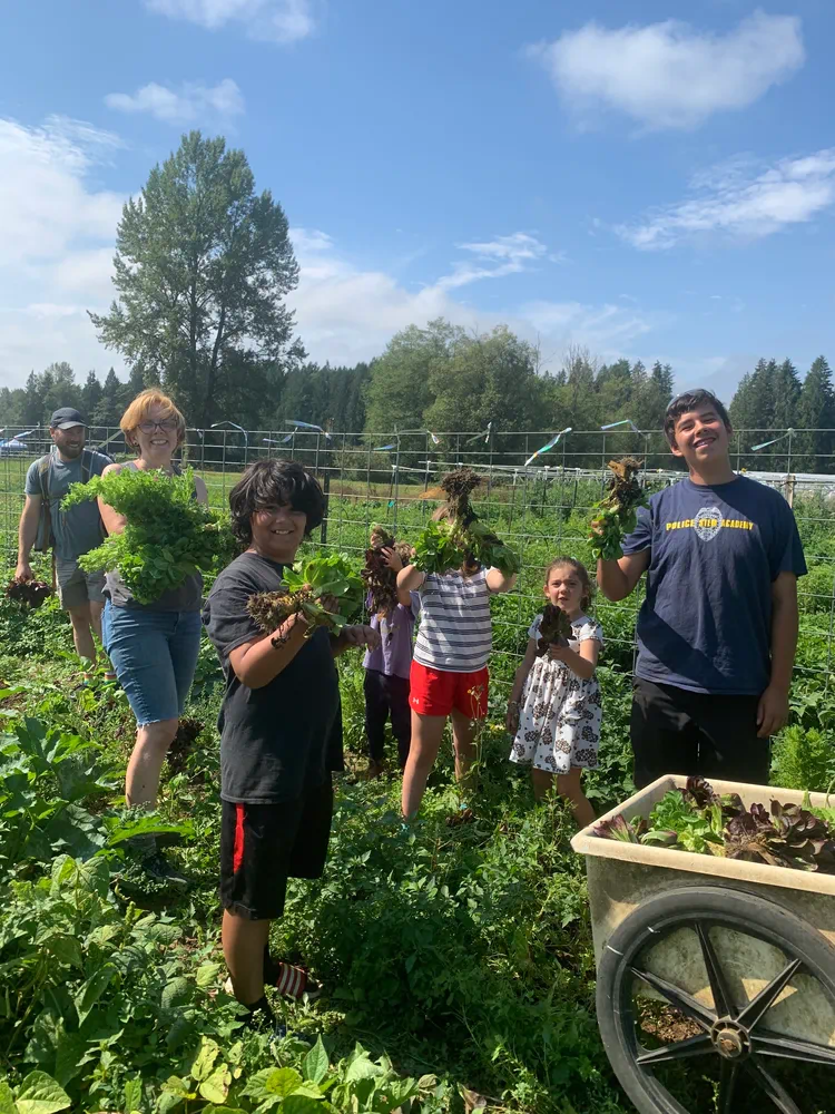 Children and adults holding freshly harvested leafy greens in a garden at Rooted Northwest.