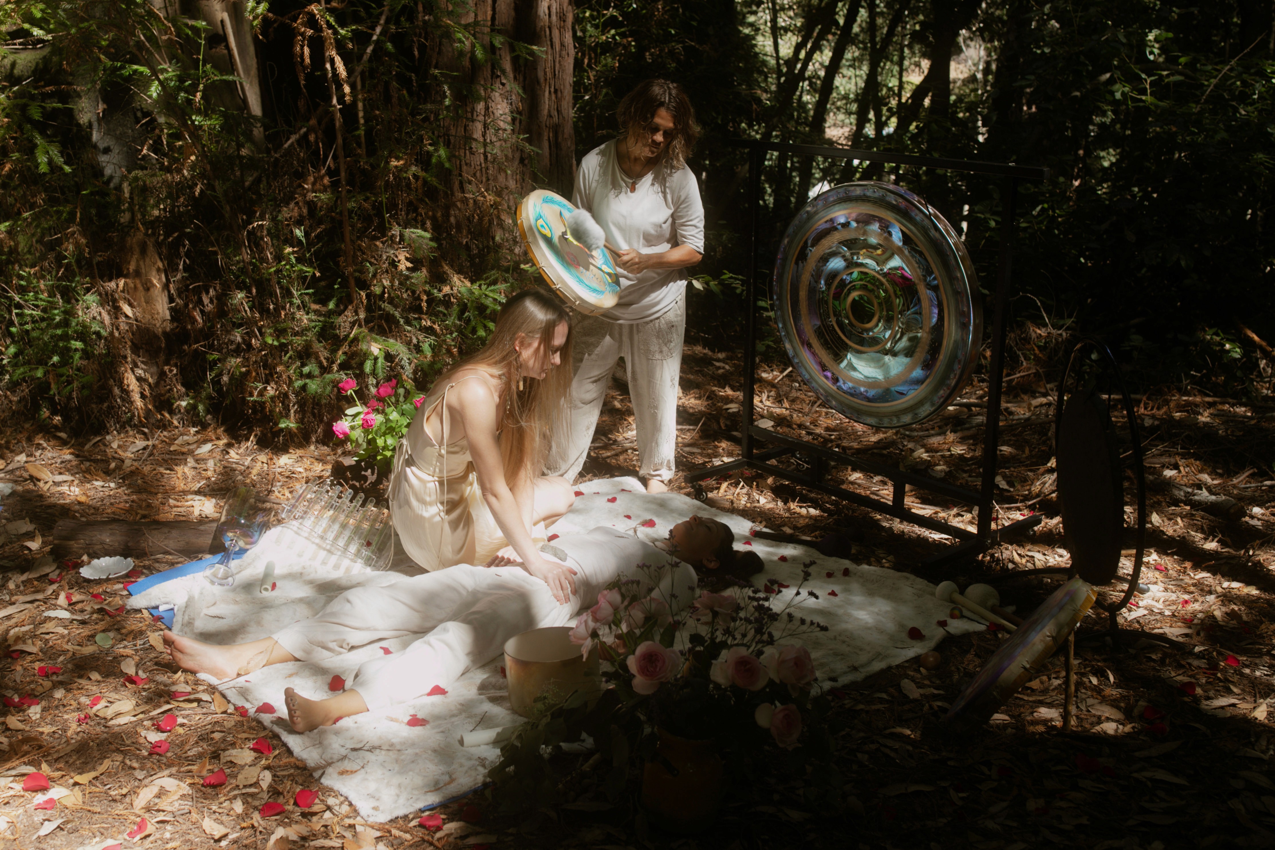 Guide performing sound healing with a gong over a participant lying on a white blanket with rose petals
