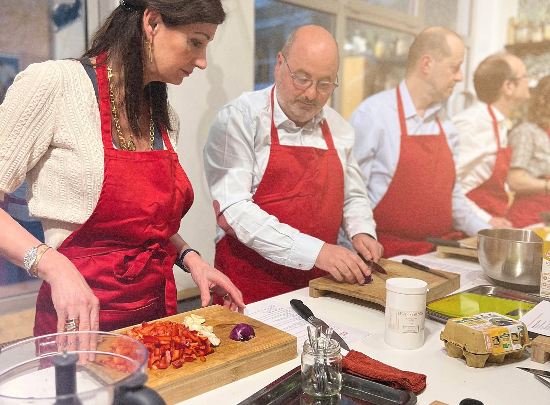 Des personnes en tablier rouge préparent des ingrédients en vue d'une activité de cuisine. Elles sont concentrées sur la coupe de légumes et l’organisation des aliments pour une recette.