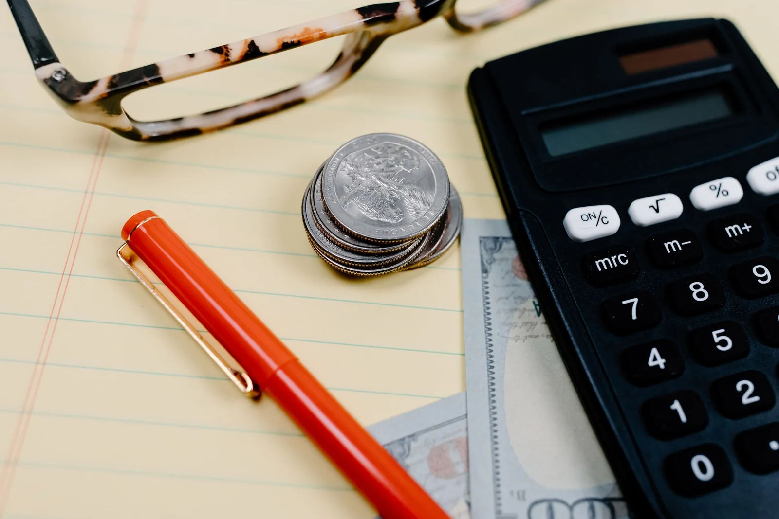 A calculator, stacked coins, and cash arranged on a budgeting notebook.