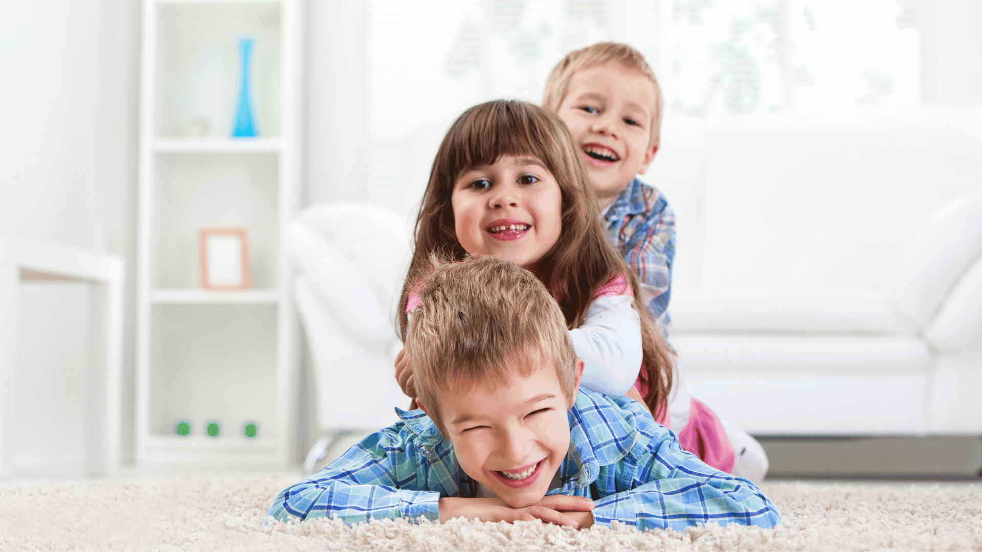 Three children lying on the floor stacked on top of each other, all smiling, relaxed, and having fun.