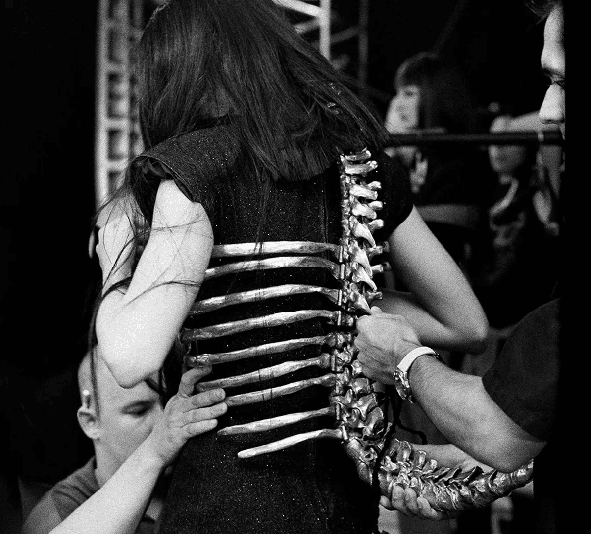 Black and white archival photo showing the fitting of the famous aluminium Skeleton Corset with a realistic spine and rib cage, designed by Shaun Leane for Alexander McQueen.