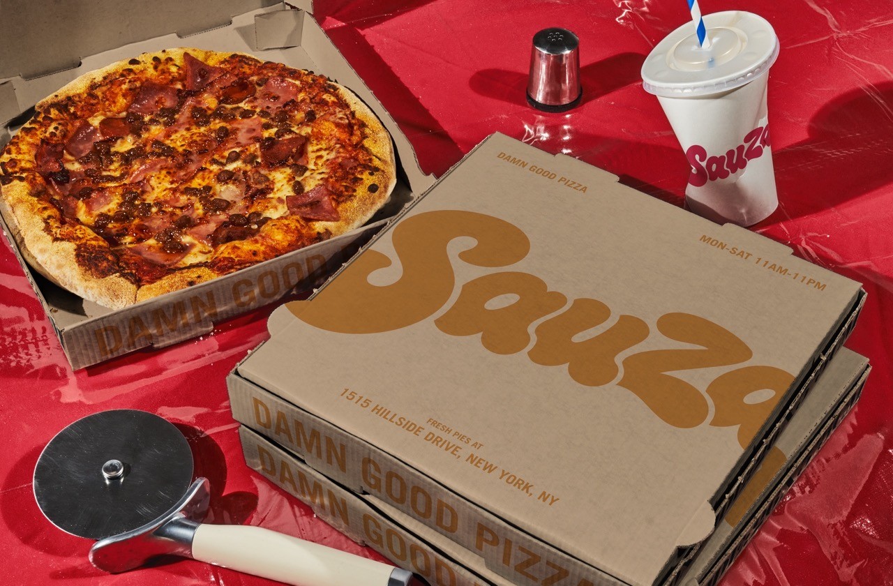 Sauza Pizzeria logo on a pizza box, surrounded by other dinner items like cups, a pizza cutter and pepper flakes.