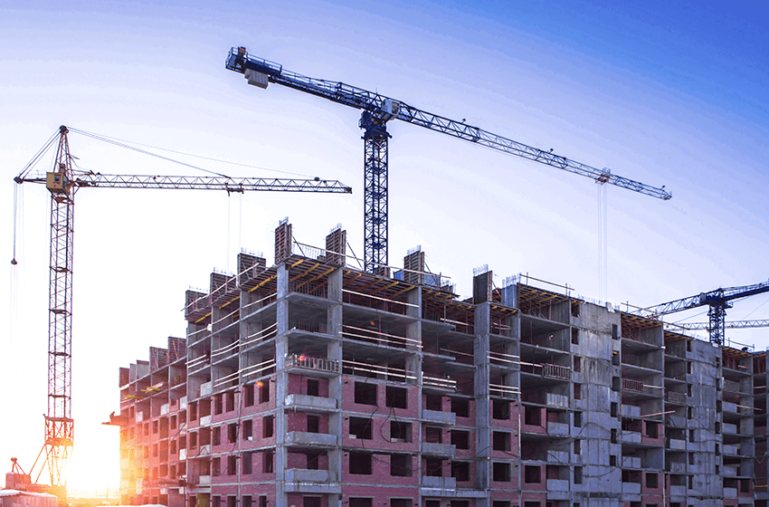 Heisekraner i soloppgang over et byggeprosjekt