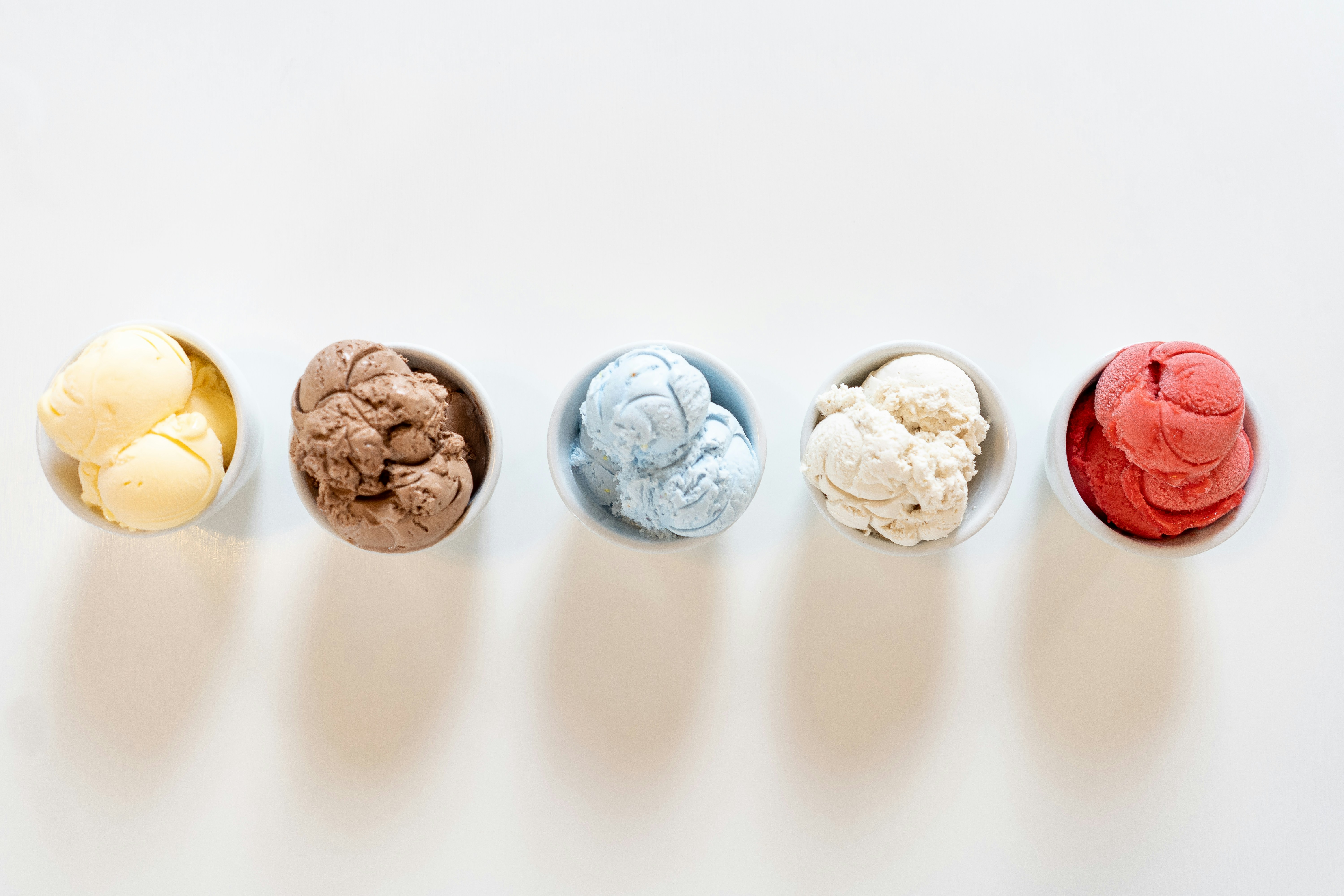 Five cups of ice cream in different flavors on a white table