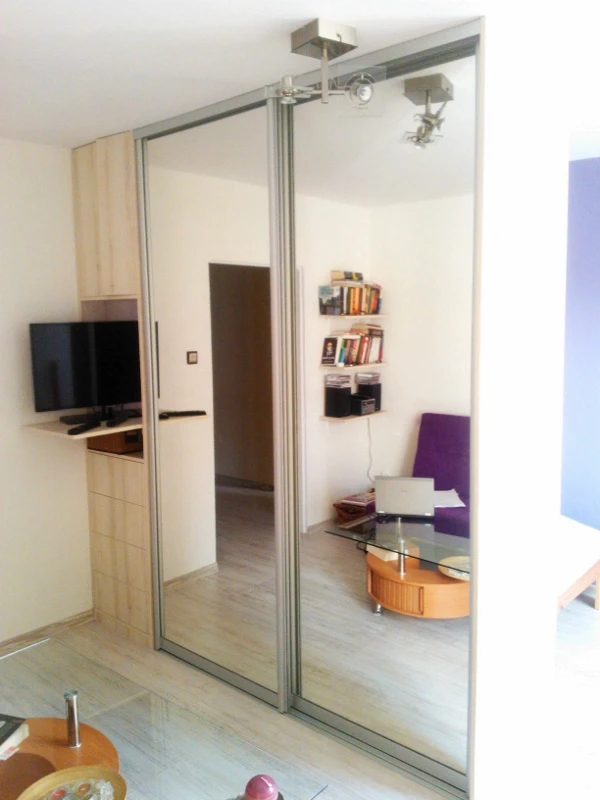 Duża szafa przesuwna z lustrzanymi frontami w aluminiowych ramkach, optycznie powiększająca przestrzeń salonu.