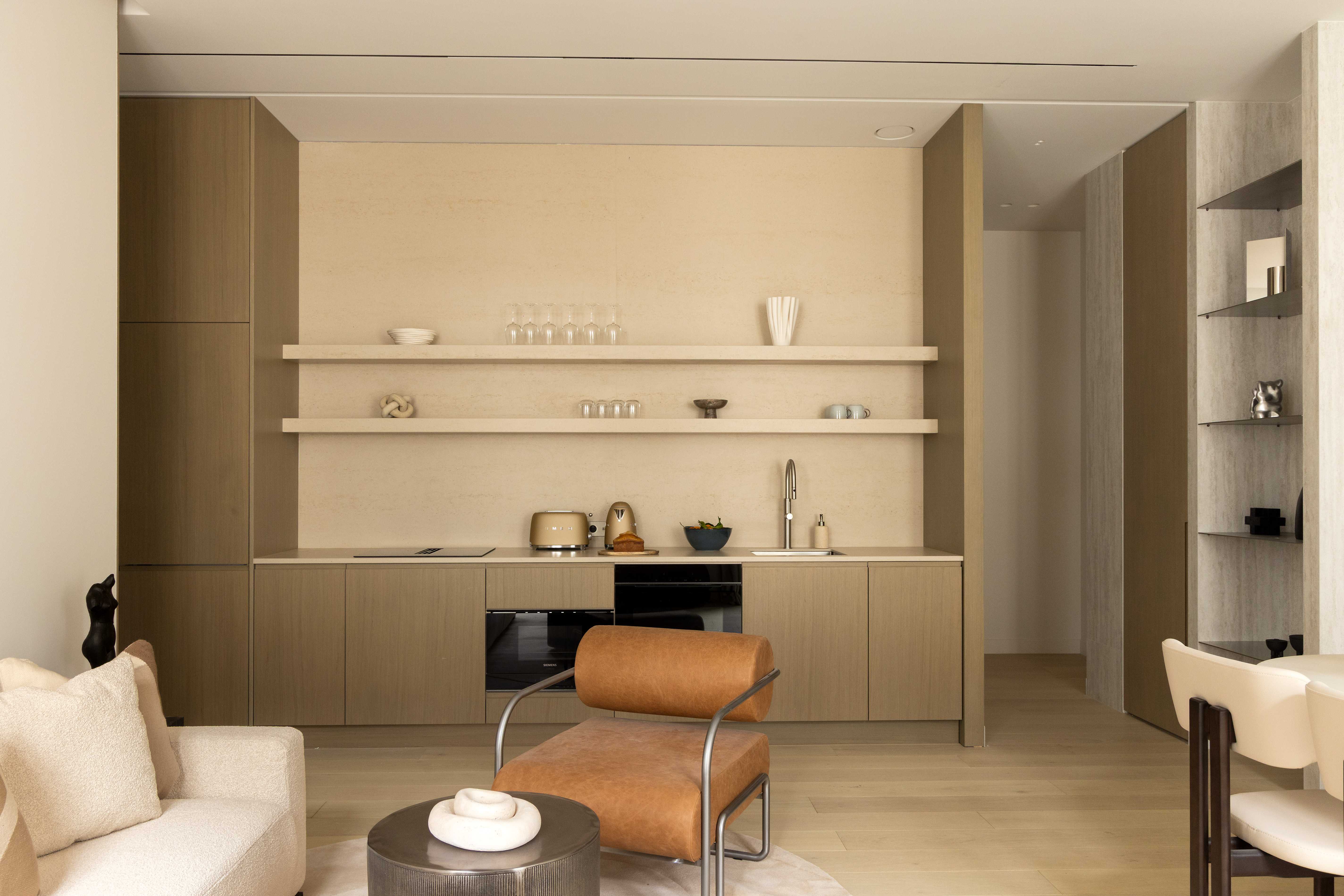 Cuisine ouverte en bois clair avec etageres, ustensiles et fauteuil cognac tubulaire au premier plan