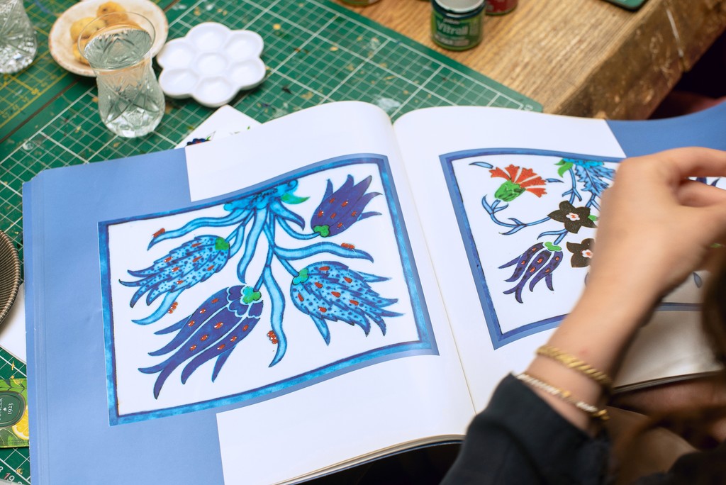 Open book of Turkish tile designs alongside a participant's work in progress at a tile painting workshop in Istanbul. Discover the art of Turkish ceramics at this popular Istanbul workshop.