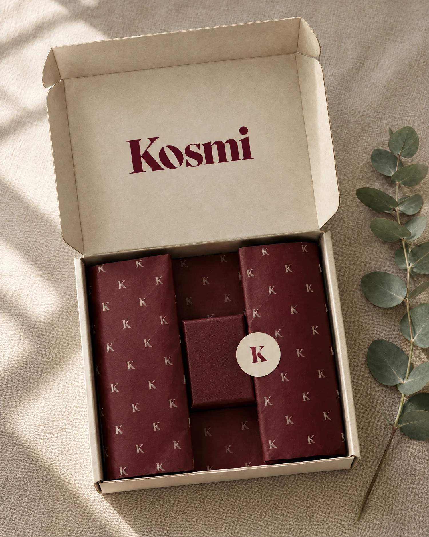 An open Kosmi mailer box with the logo inside the lid, cherry K-pattern tissue and a K sticker.