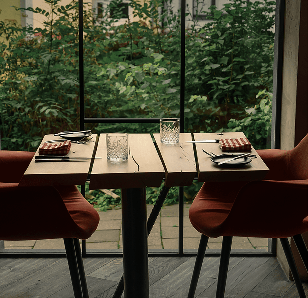 Stylově prostřený stůl v moderní restauraci s červenými židlemi a výhledem do zeleně.