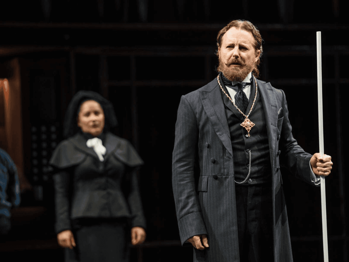 Man in formal costume holding a staff onstage in a dramatic Twelfth Night scene.