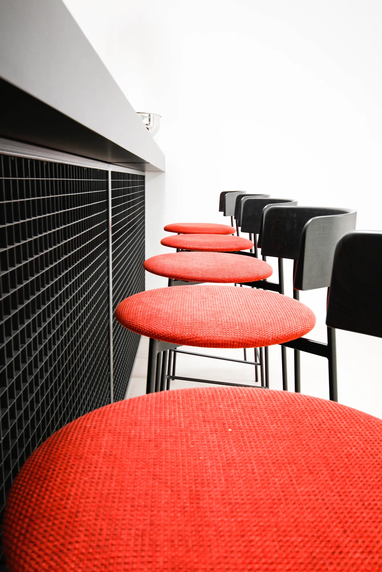 Row of bar stools with red round seats along the black bar counter.