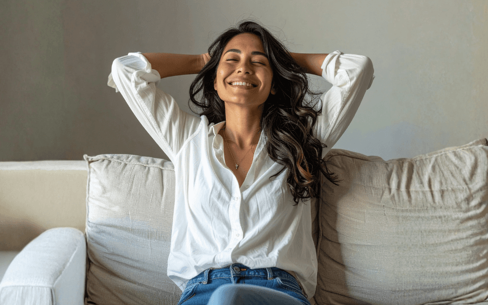 Woman relaxing on a sofa with her hands behind her head, representing financial flexibility and less stress with Kina payments