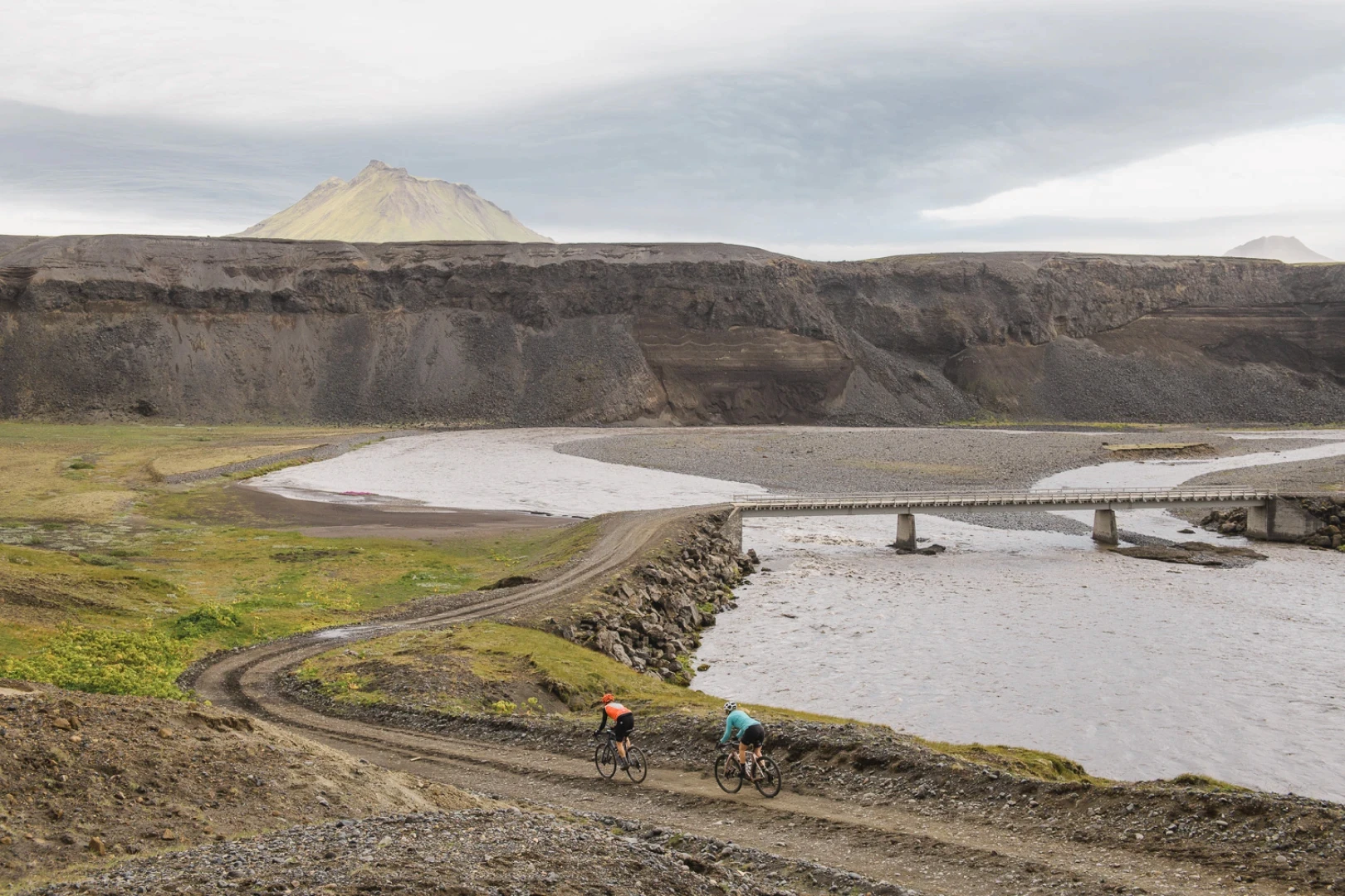 Two gravel riders ride towards a bridge in the highlands of Iceland