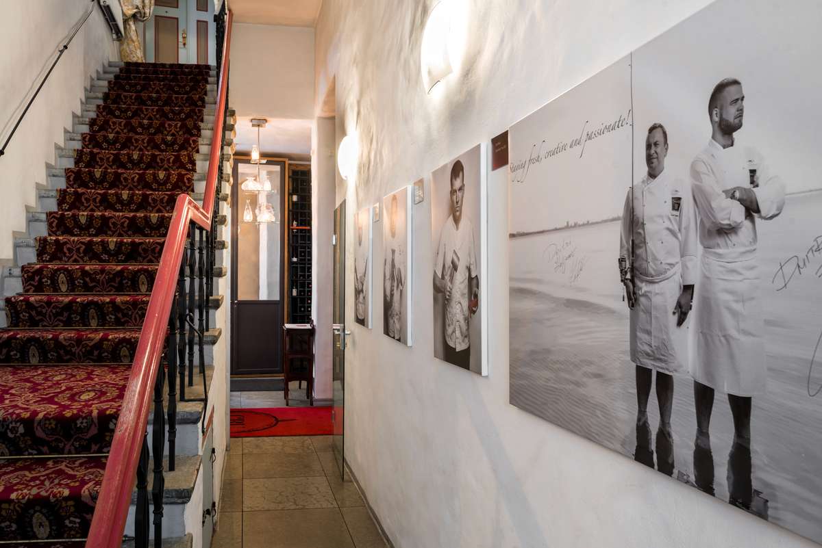 Elegant interior hallway featuring a grand staircase and gallery walls displaying black and white photographs under bright lighting.