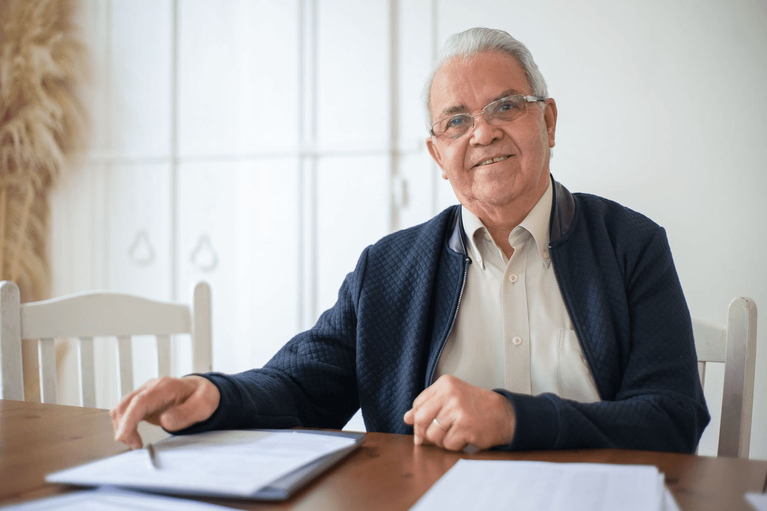An older man at his dining table with a folder of paperwork open in front of him.