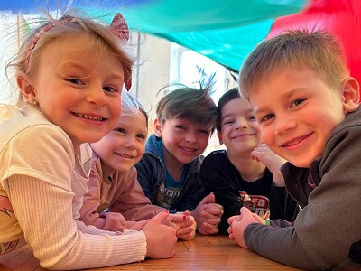 Skupina dětí sedící u stolu ve třídě a dívající se do objektivu