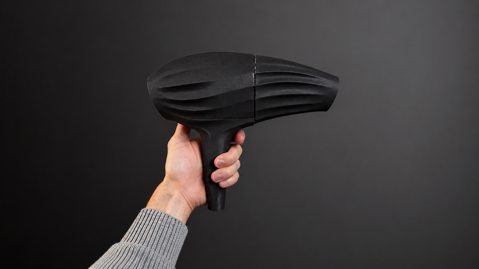 A hand holding a matte black model of the Neuro dryer, the grip ridges cut into its housing.