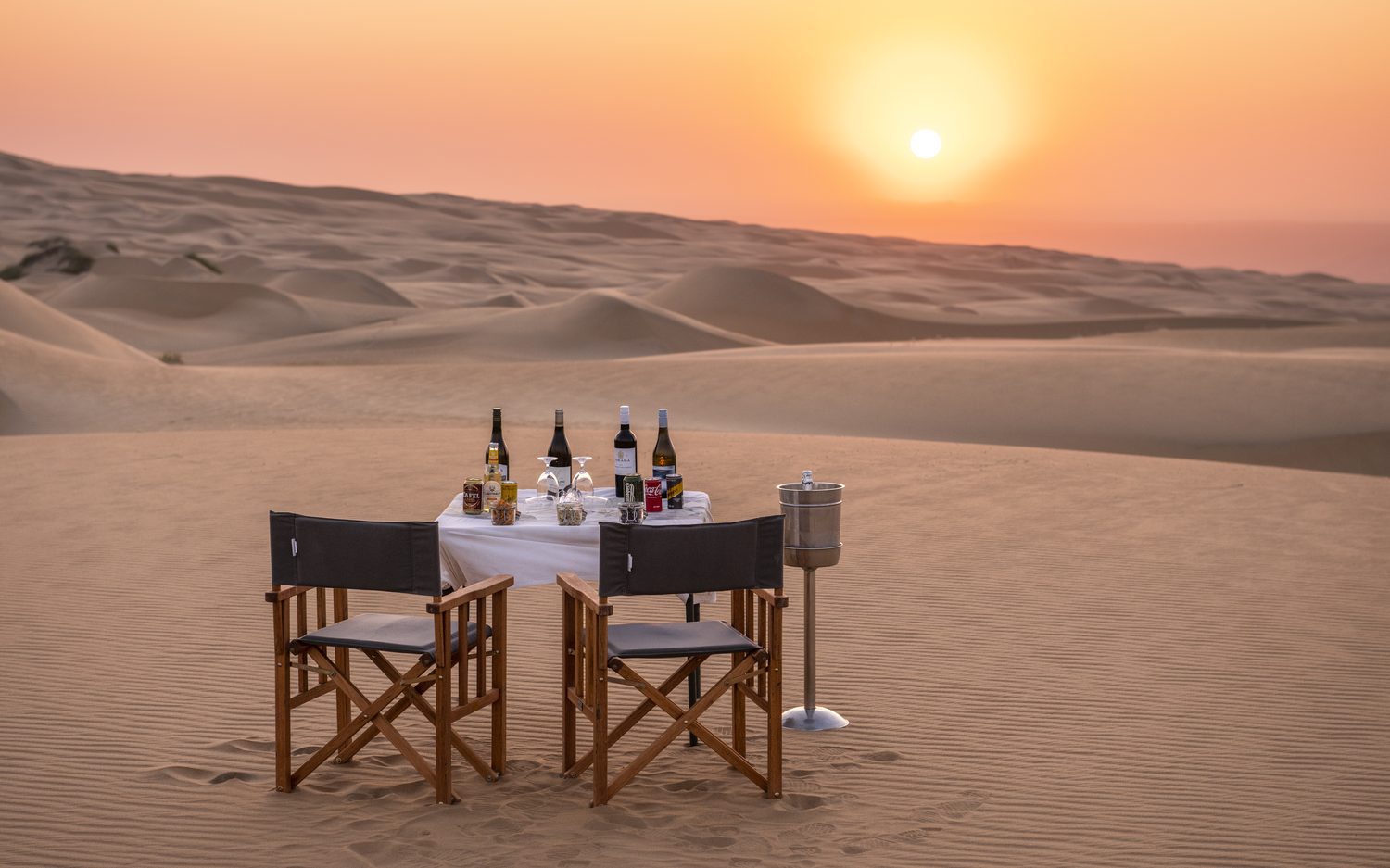 A table for two set on a dune as the desert sun goes down