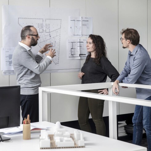 Black and white photo of two people looking at a computer screen with papers on wall