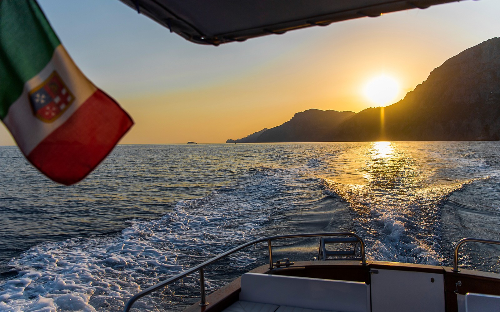 Båtkryssning längs Amalfikusten vid solnedgången med italiensk flagga.