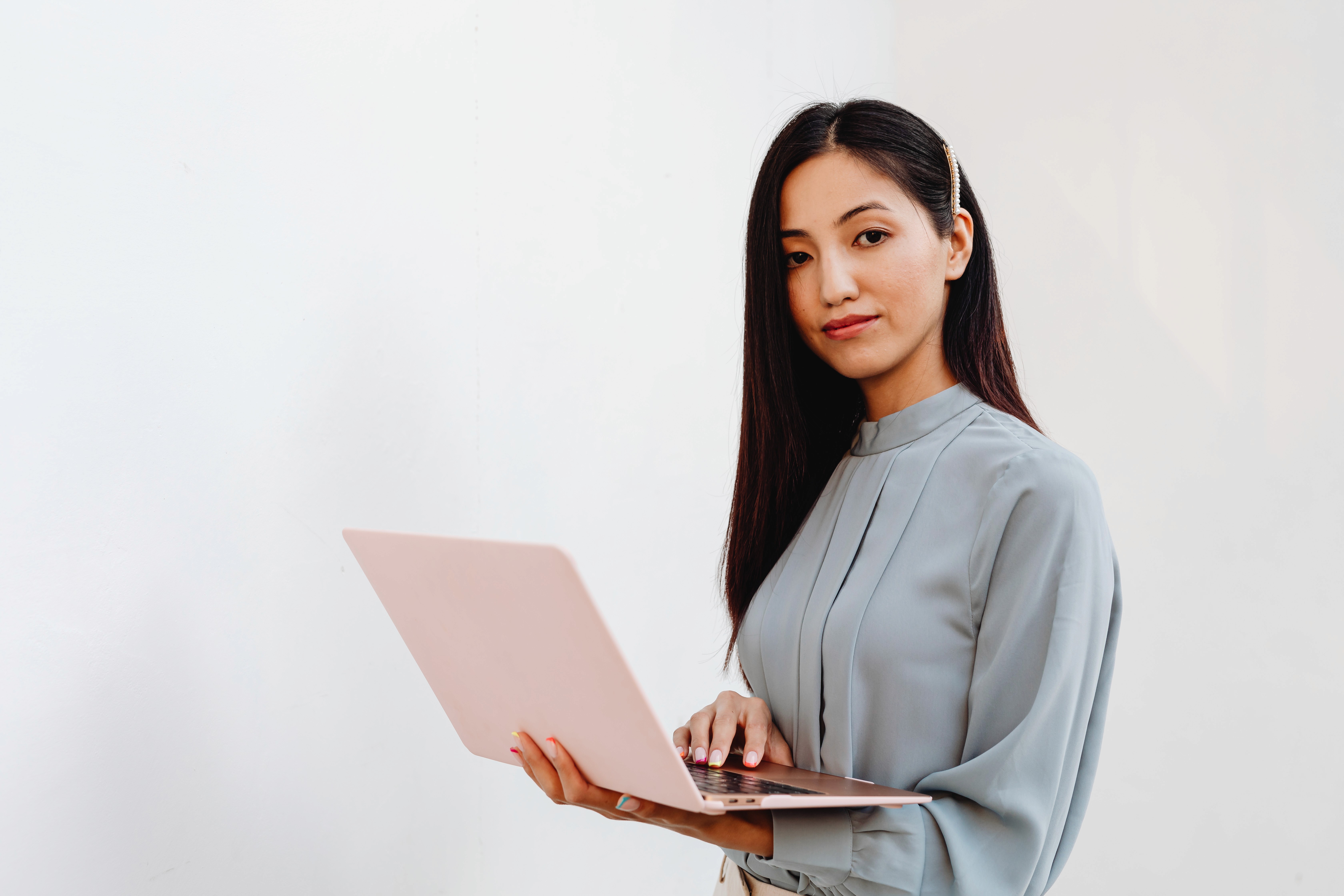 A professional woman with long dark hair holding a pink laptop against a plain white background.