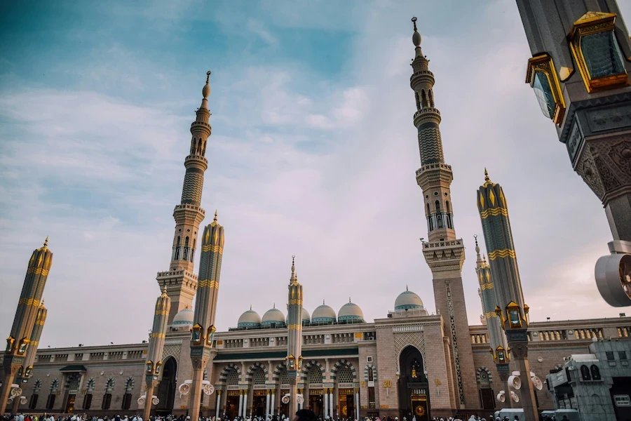 Grand Saudi mosque courtyard with tall minarets and domes under a soft blue sky.