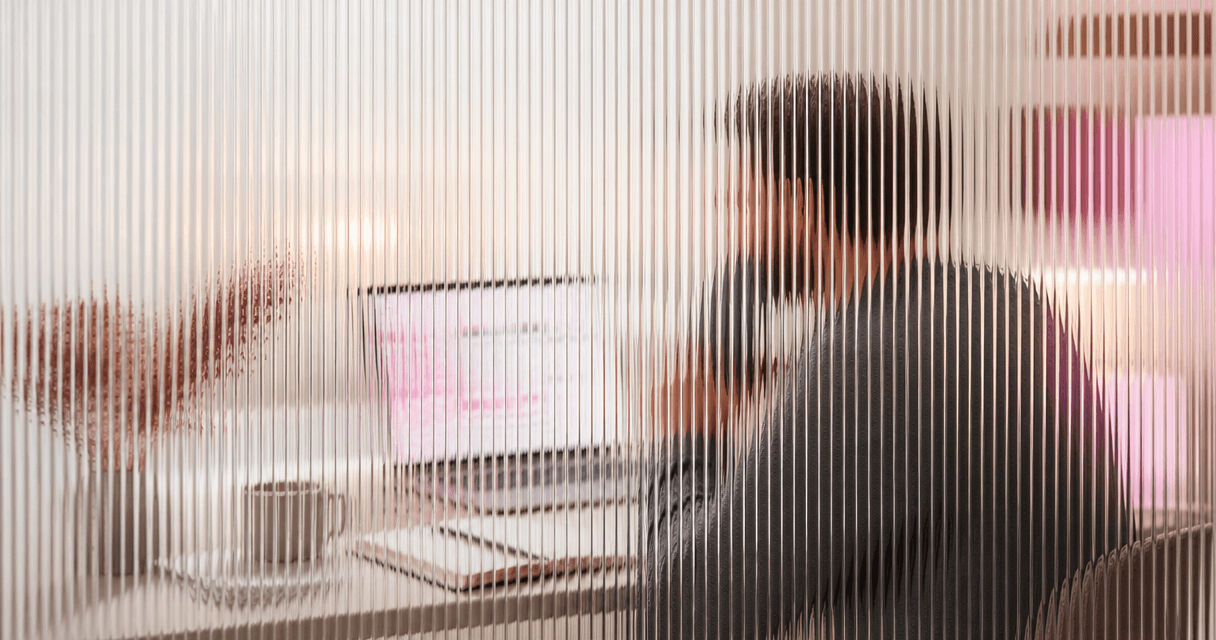 Salesperson reviewing a CRM pipeline on a laptop with phone in hand, seen through vertical fluted glass