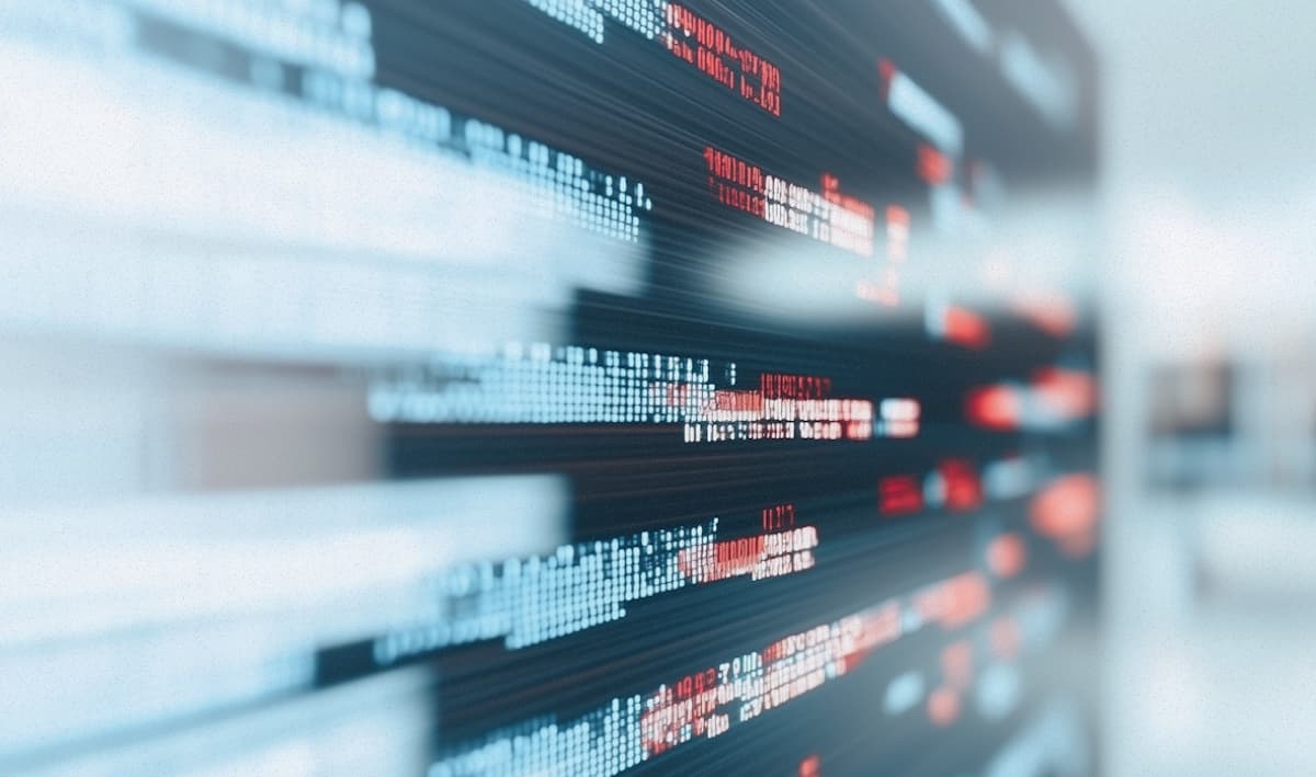 A man sits facing away from us at a desk with multiple monitors