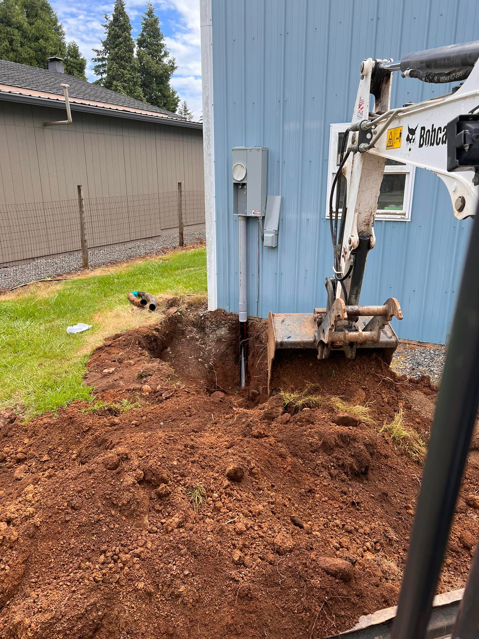 Bobcat digging dirt for drainage solution at a residential property in Oregon City