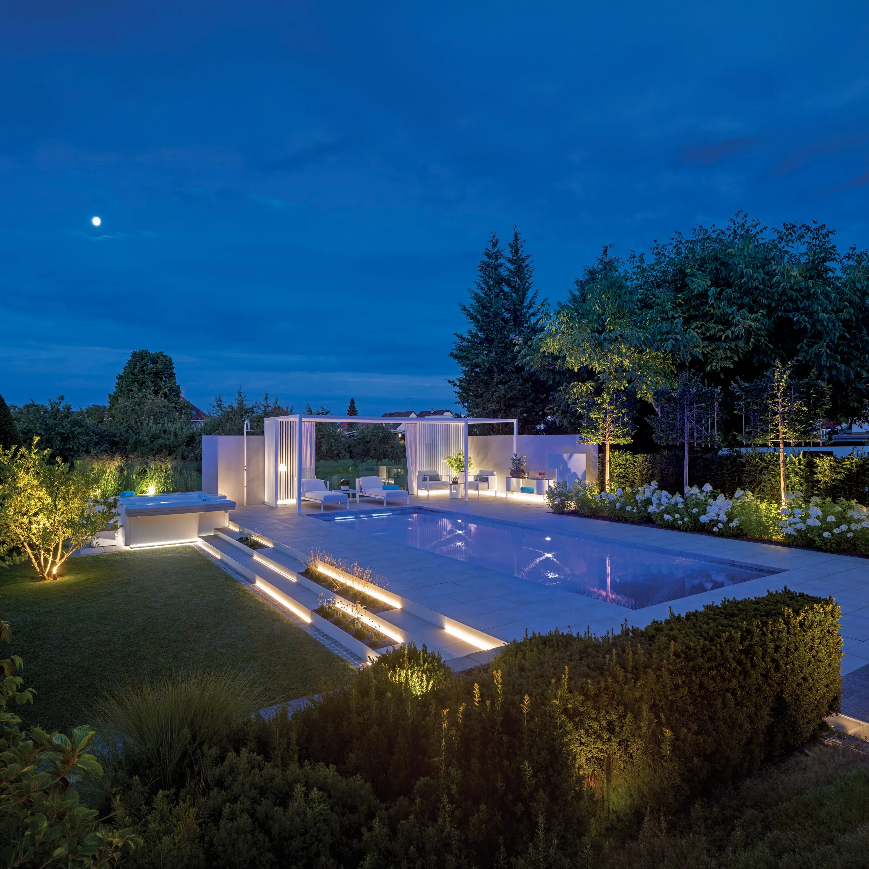 MLine swimming pool at night with illuminated steps, white pergola, and landscaped garden