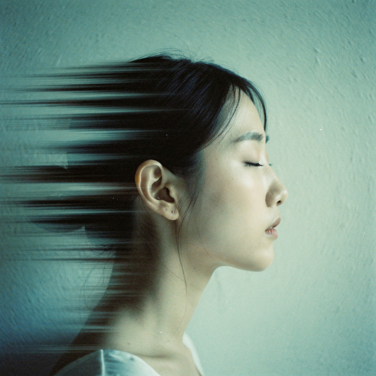 Profile of a woman with closed eyes, dark hair in a bun, facing right. Motion blur effect streams from her face, creating a serene, contemplative mood.