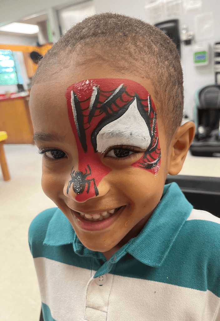 Smiling young boy with vibrant Spider-Man face paint in an indoor setting, featuring a colorful and playful atmosphere